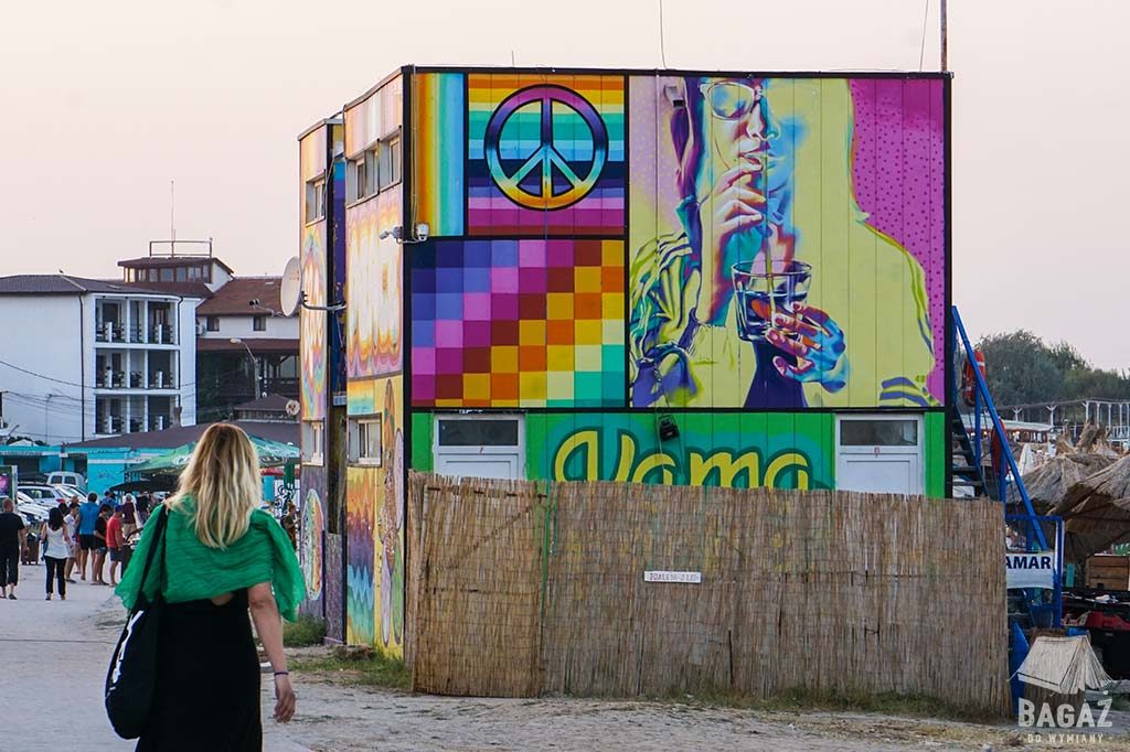 kobieta idąca w stronę kolorowych graffiti namalowanych na barach plażowych w vama veche